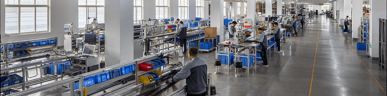 View down a factory walkway showing multiple assembly benches with people building welding torches, demonstrating the scale of the facility.