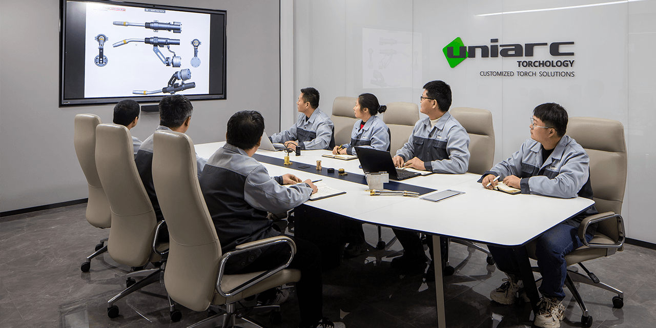 Uniarc Group team in a meeting room reviewing a welding torch design on screen, with products on the table and the company logo on the wall.